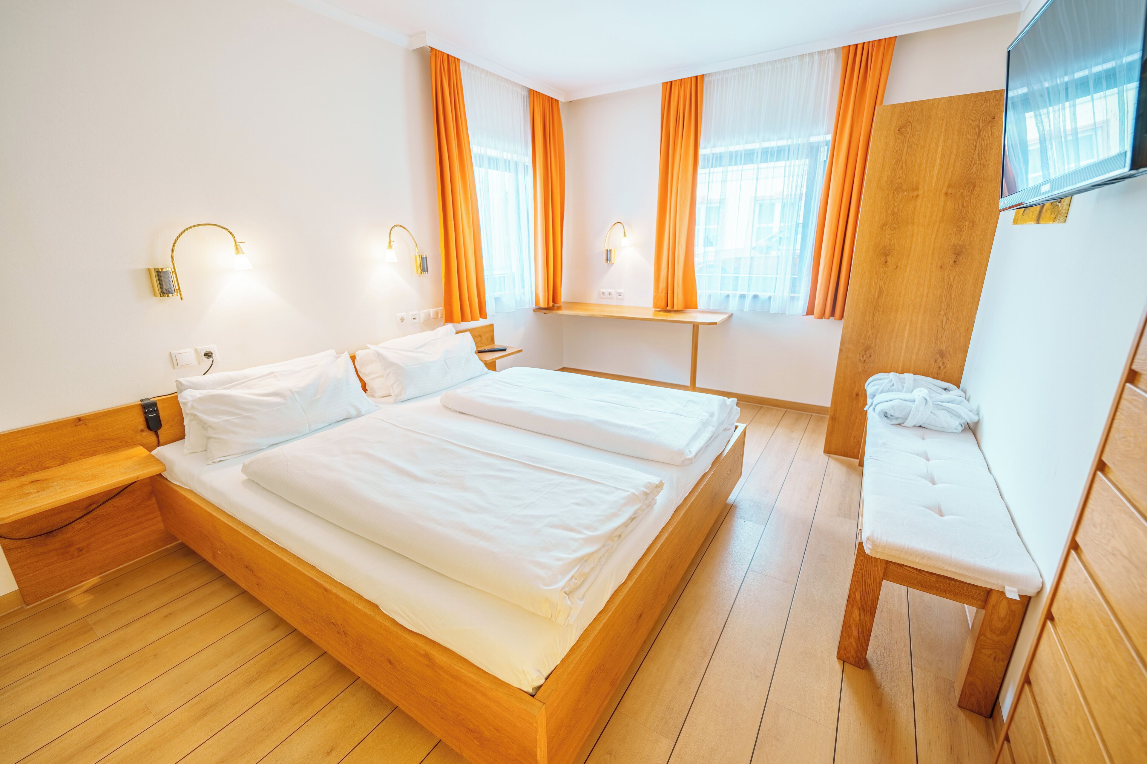A hotel room with a wooden bed, a bench, a TV, and a window with curtains.