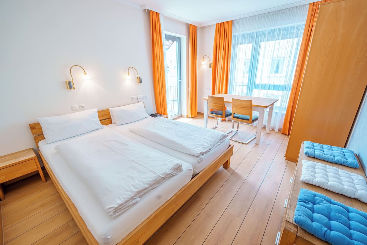 Une chambre d’hôtel avec un grand lit, un bureau et une chaise, des rideaux orange et une vue sur l’extérieur.