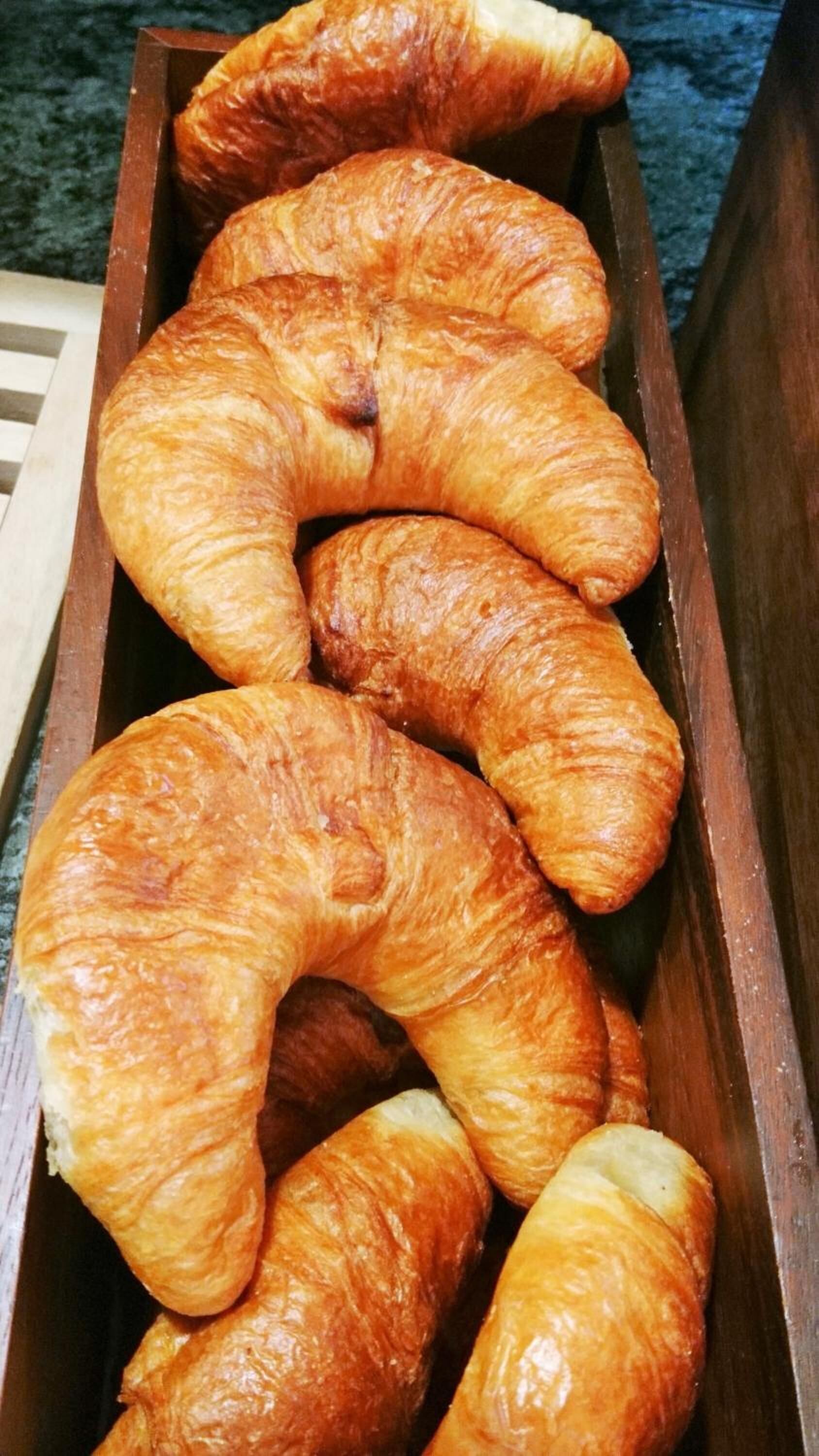 A wooden box containing several golden-brown croissants.