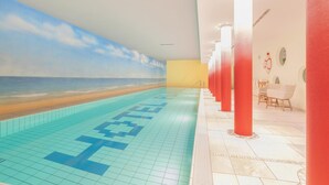 Ein Schwimmbecken mit Strandbild auf einer Seite, roten Säulen und einer Sitzgelegenheit mit Tischen und Stühlen.