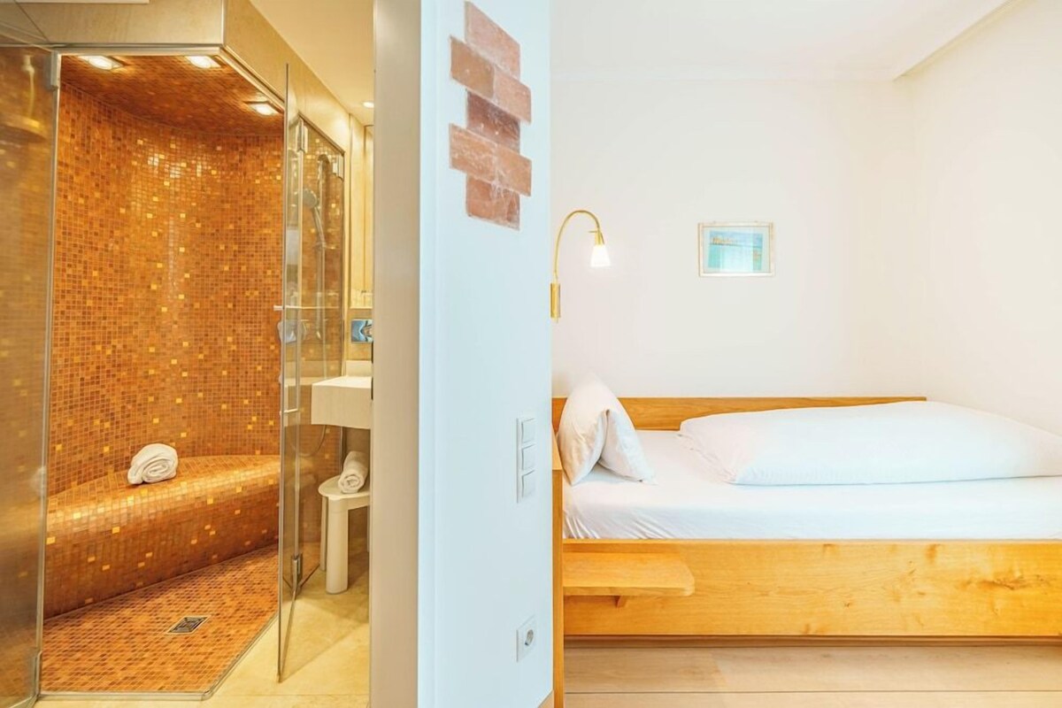 A modern bathroom with a glass shower enclosure and a wooden bed with white bedding.