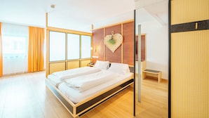 Ein modernes Schlafzimmer mit einem großen Bett, Holzboden und Blick auf die Stadt durch große Fenster.