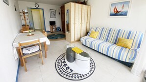 Ein Wohnzimmer mit einem gestreiften Sofa, einem Esstisch mit Stühlen, einem Fernseher und einem Kleiderschrank.