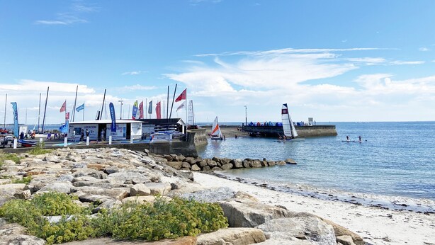 Ein Yachthafen mit mehreren angedockten Segelbooten, einer anlegenden Mole und einem Gebäude mit der Aufschrift "Location".