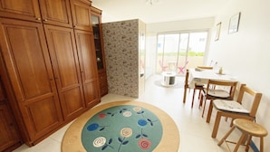 Ein Zimmer mit einem Holzschrank, einem Esstisch mit Stühlen, einem gemusterten Teppich und Blick durch eine Glastür.
