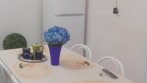 Een eethoek met een witte tafel, blauwe bloemen en een televisie aan de muur.