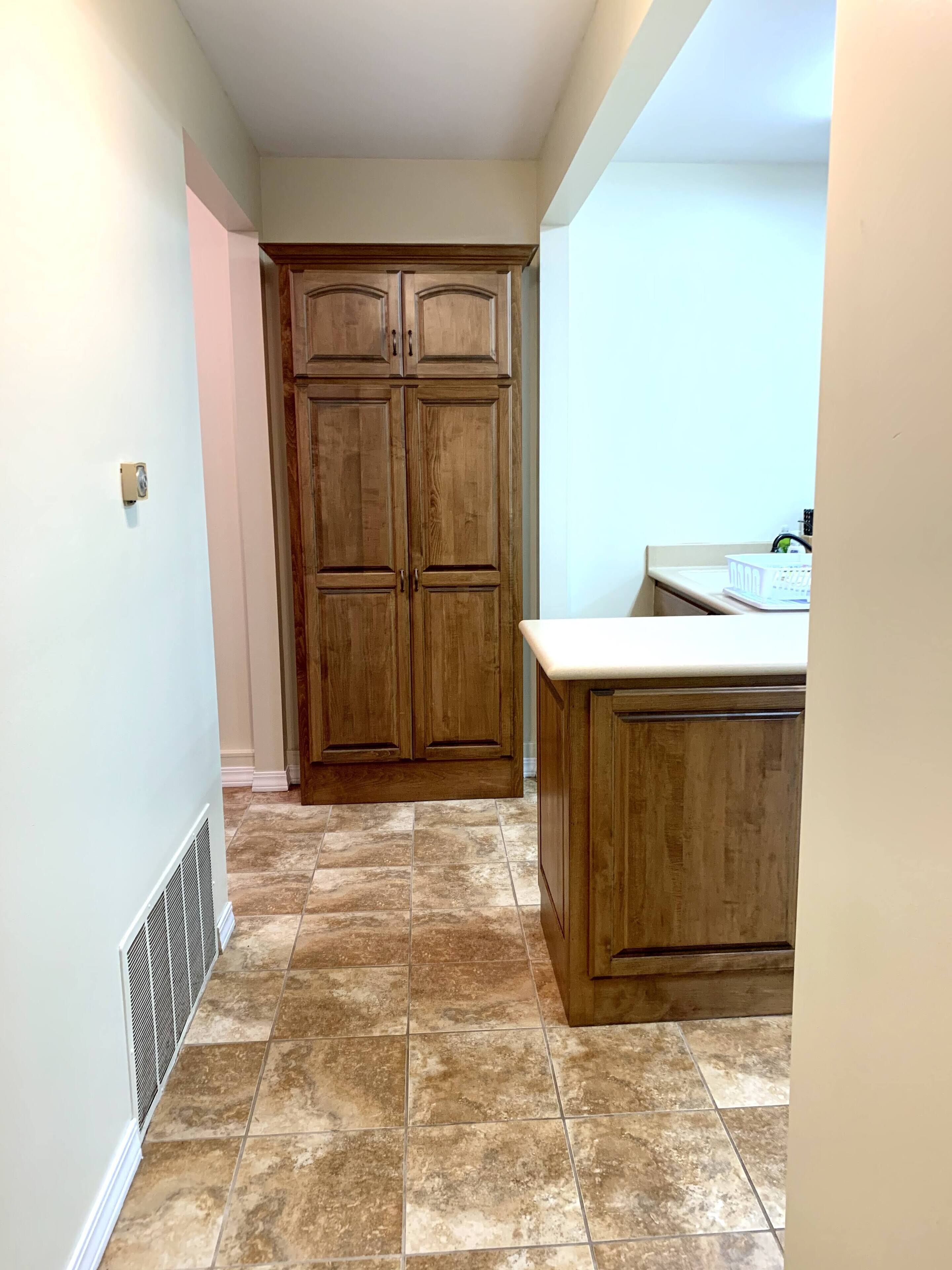 A kitchen with wooden cabinets, a countertop, and a vent on the wall.