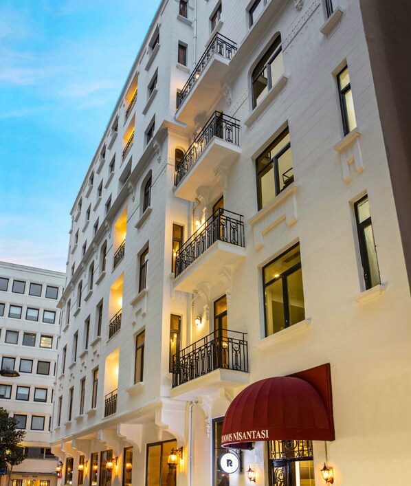 A multi-story hotel with balconies, a red awning, and illuminated windows. - The Rooms Nisantasi (Istanbul)
