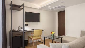 A compact living space with a kitchenette, a sofa, a small table, and a TV mounted on the wall.