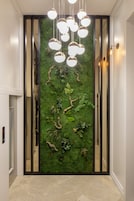 Un corridoio con una parete verde decorata da piante e un moderno apparecchio di illuminazione.