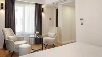 A hotel room with two armchairs, a small table with a vase of flowers, a bed, and a window with curtains.