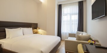 Ein Hotelzimmer mit einem großen Bett, einer Couch, einem an der Wand montierten Fernseher und einem Fenster mit Vorhängen.
