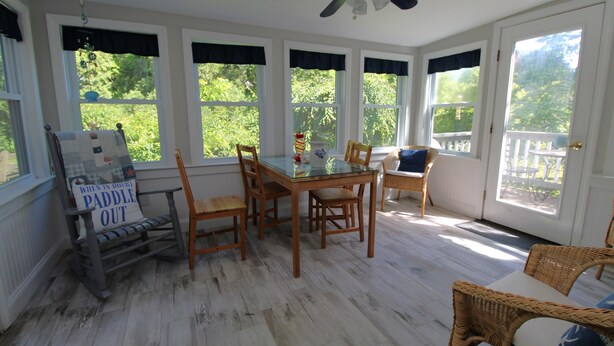 Un porche cubierto con una mesa de comedor, sillas y un letrero que dice 'WHEN IN DOOMED PADDLE OUT'.