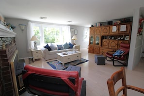 Un salon comprenant un canapé, une table basse, un fauteuil en cuir rouge, une cheminée et un meuble en bois orné de cadres avec des photos.