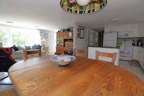 Un comedor con una mesa de madera, sillas, un tazón y una cocina al fondo.