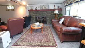 Una sala de estar con chimenea, sofá de cuero, sillones y una alfombra estampada.