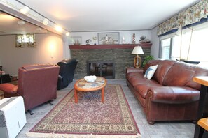 Una sala de estar con chimenea, sofá de cuero, sillones y una alfombra estampada.