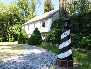 Ein Haus mit Kiesauffahrt, einem schwarz-weiß gestreiften Leuchtturm und umgebender Bepflanzung.