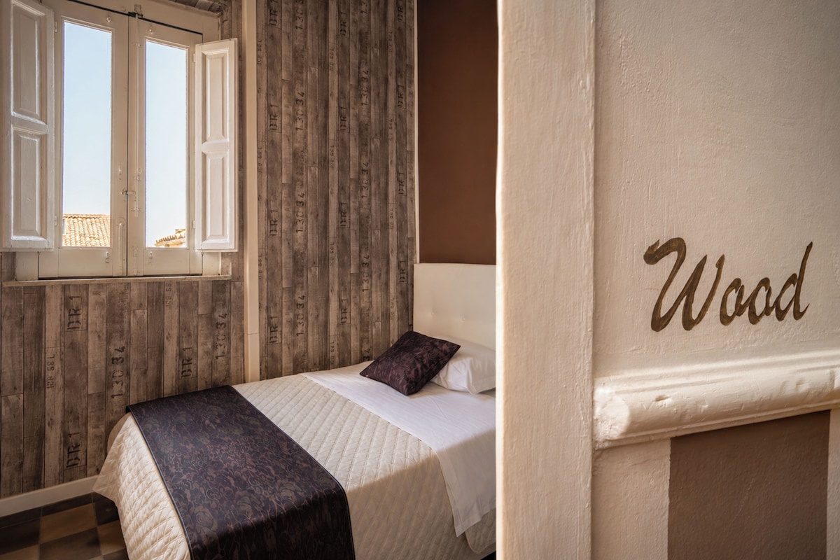 Quarto com cama, janela e parede com a palavra 'Wood'.