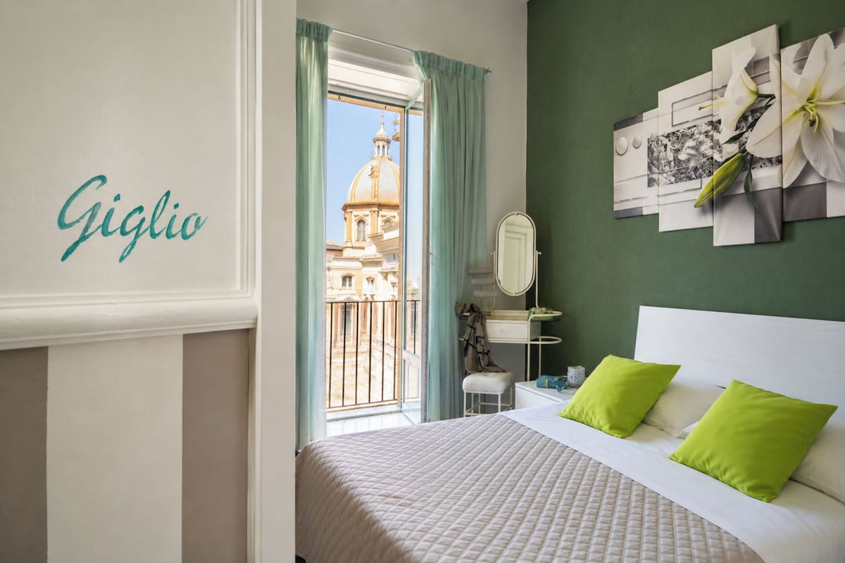 Quarto de hotel com cama, espelho, penteadeira e vista para um edifício pela janela.