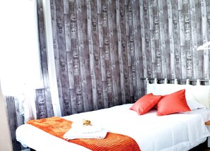A hotel room with a bed, orange and white bedding, and a wooden wall with numbers.
