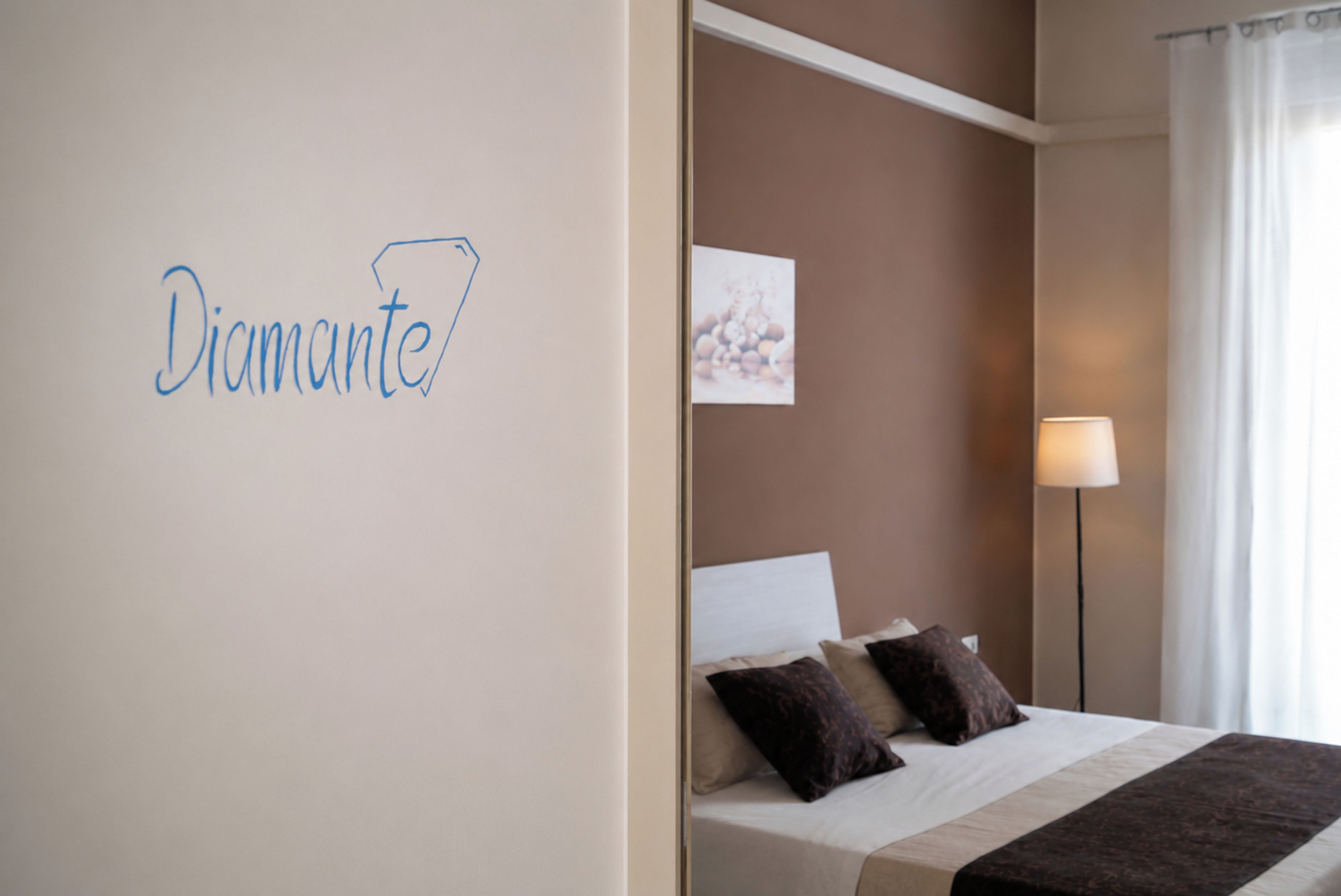 Ein Hotelzimmer mit Bett, Kissen, Nachttisch, Lampe und einer Wand mit dem Schriftzug 'Diamante'.