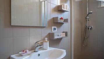 A bathroom with a sink, mirror, shelves with toiletries, and a shower.