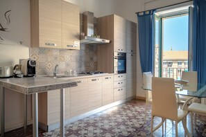 A modern kitchen with a gas stove, oven, and a dining area with a glass table and chairs. - I Colori della Sicilia (Caltagirone)