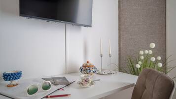 Ein ordentlich eingerichteter Schreibtisch mit einem darüber montierten Fernseher, einer Vase mit weißen Blumen und einem Stuhl.