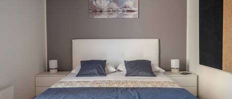 A neatly made bed with a patterned bedspread, two pillows, and a nightstand with a lamp.