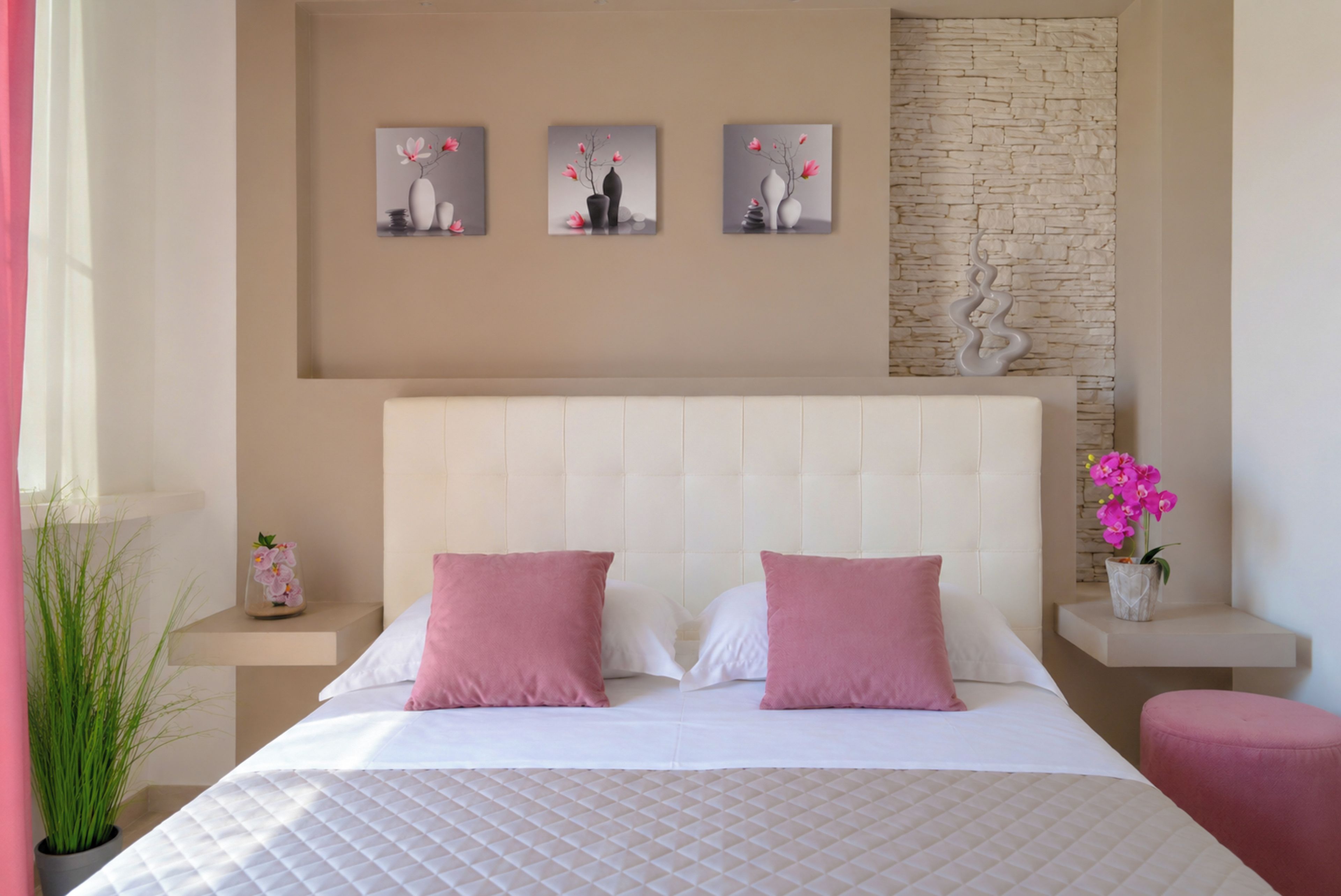 Un dormitorio ordenado con una cama grande, dos almohadas, un cabecero y tres cuadros colgados en la pared.