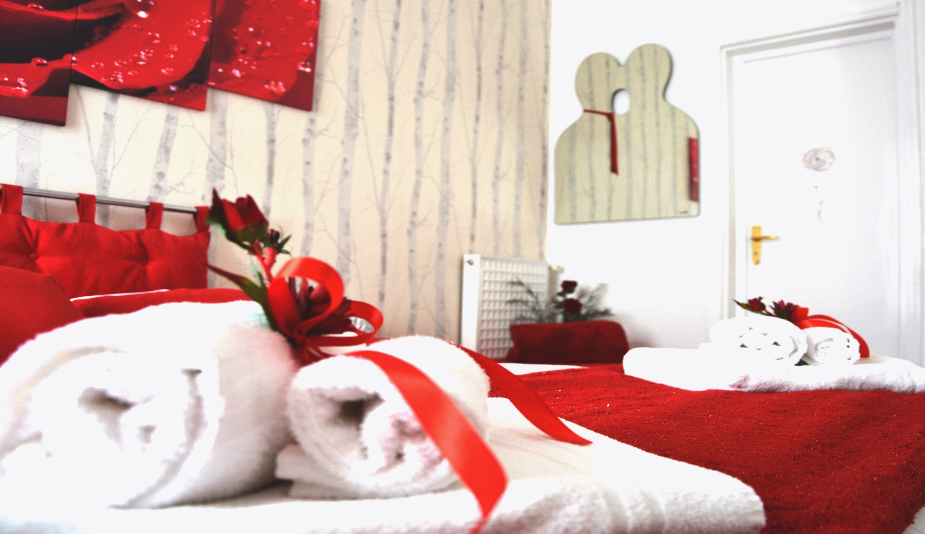 Camera d'albergo con un letto, asciugamani rossi, una coperta rossa e uno specchio fissato alla parete.