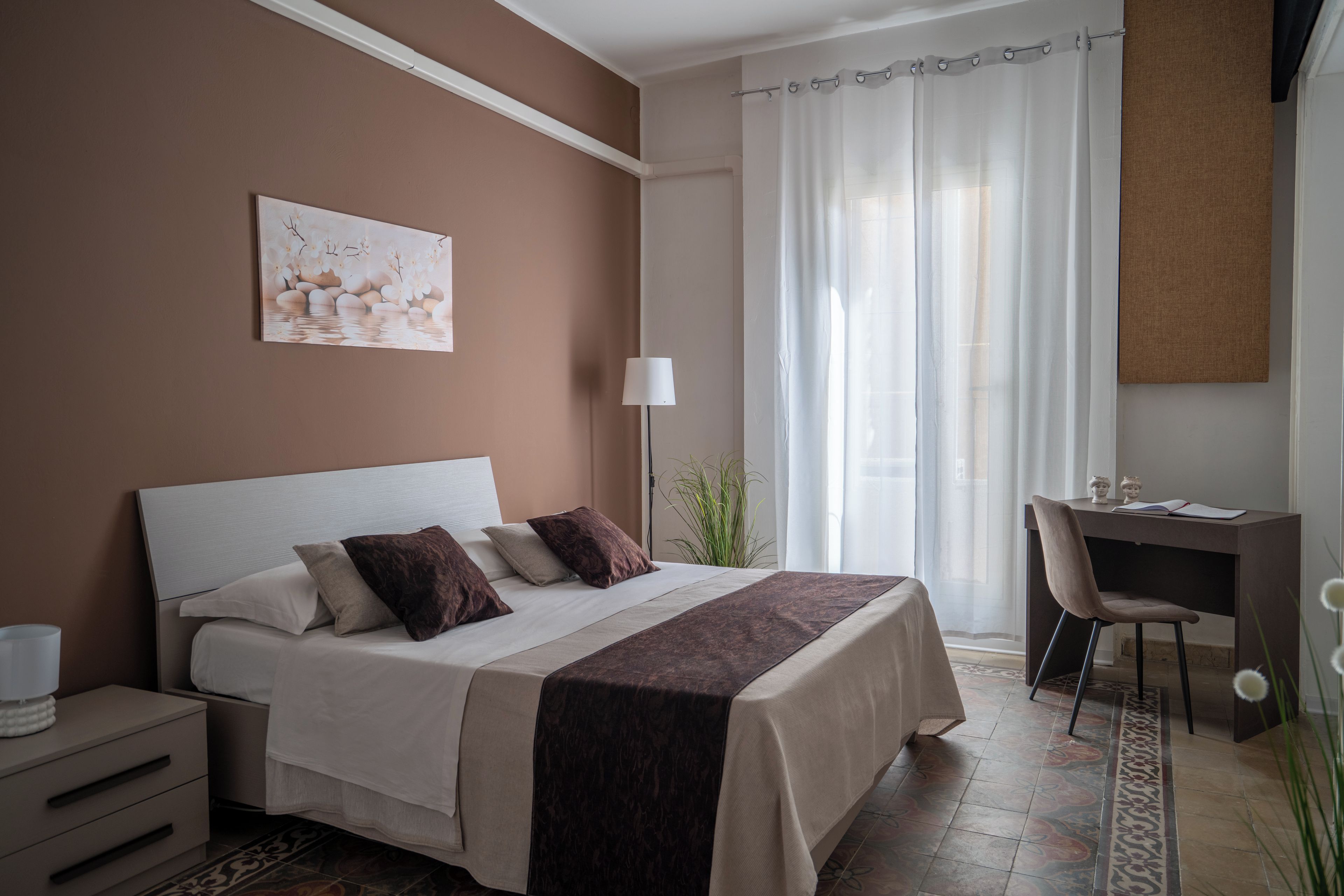 Ein Schlafzimmer mit Bett, Nachttisch, Schreibtisch, Stuhl und einem Fenster mit Vorhängen.