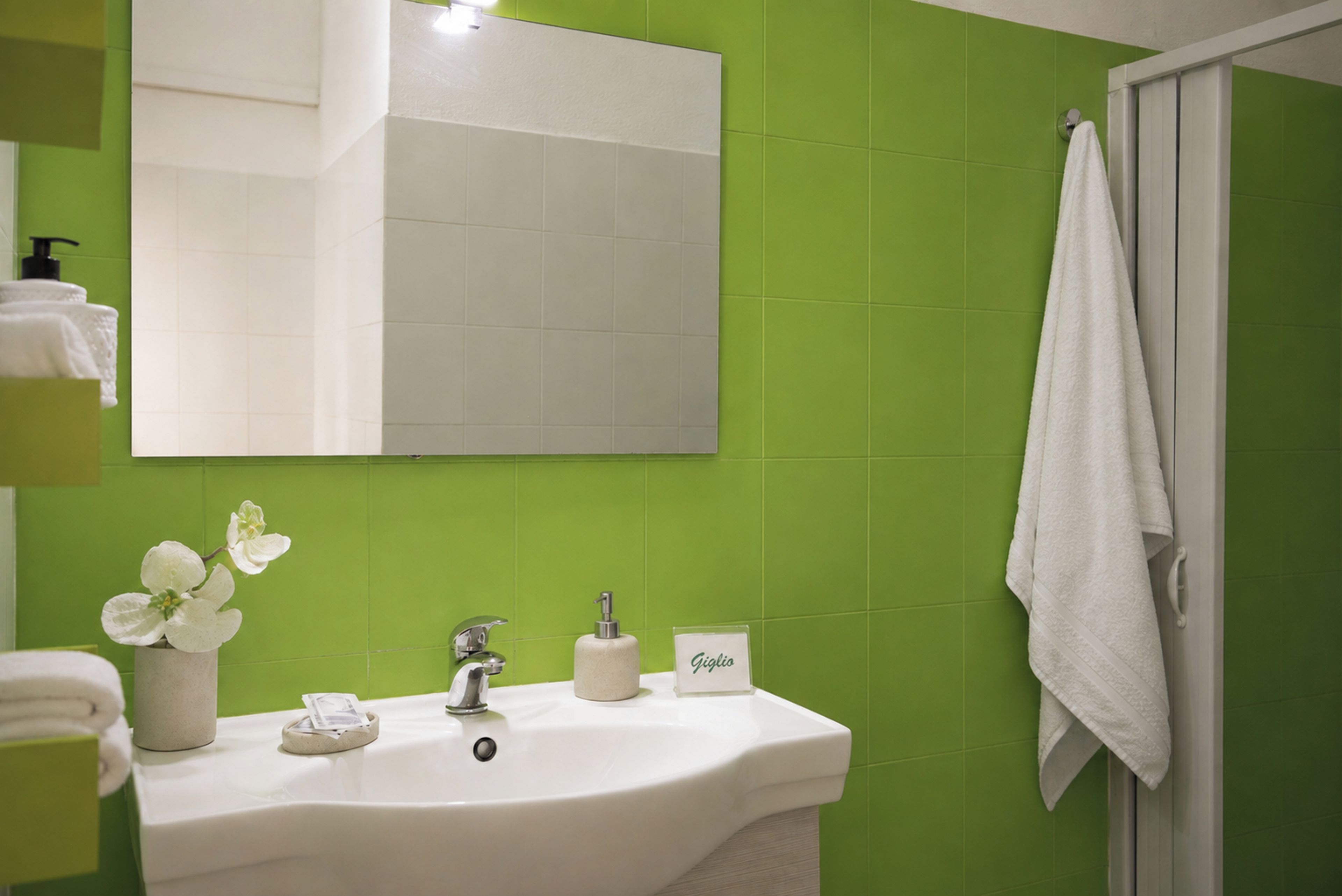A bathroom with a white sink, green walls, a mirror, and a white towel hanging on the door.