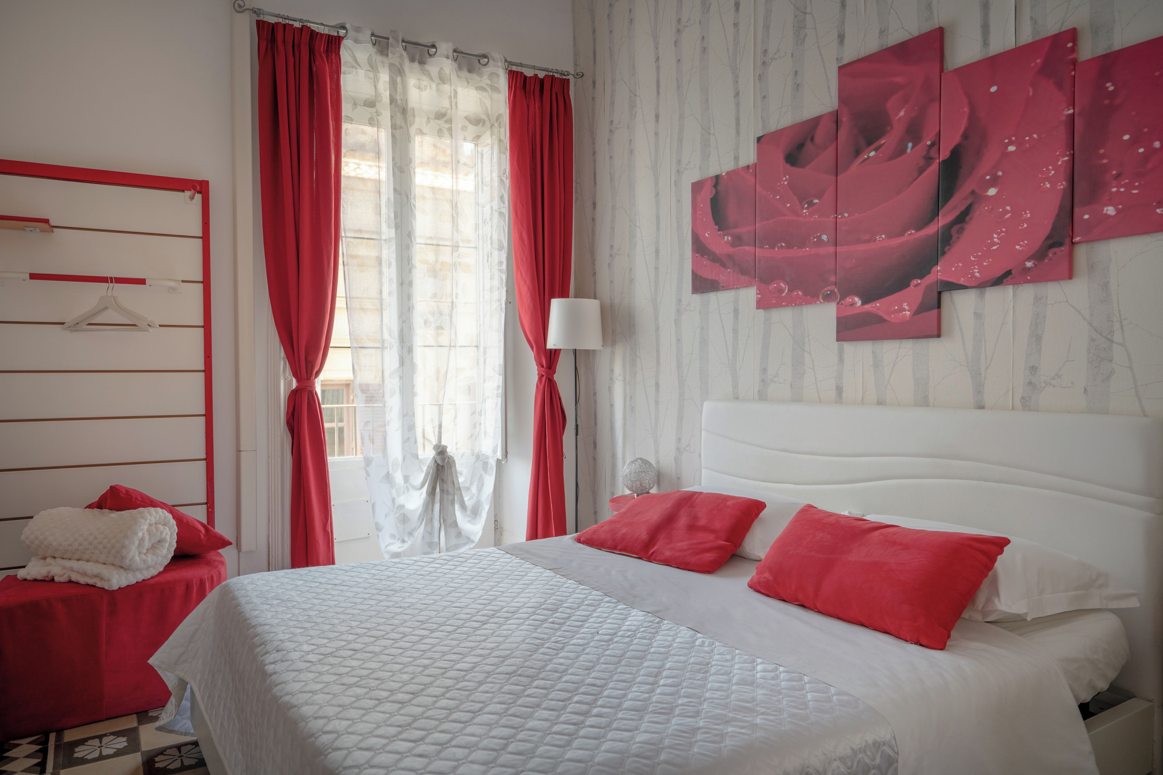 Une chambre d’hôtel avec un lit, des rideaux rouges, une tête de lit blanche et un mur orné d’un tableau abstrait rouge.