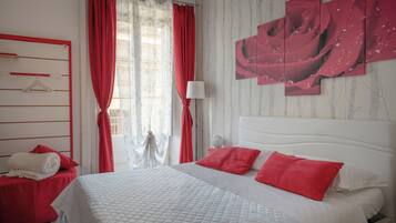 Une chambre d’hôtel avec un lit, des rideaux rouges, une tête de lit blanche et un mur orné d’un tableau abstrait rouge.