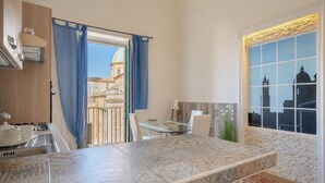 A modern kitchen with a dining area, a view of a building with a dome, and a window with a stone facade. - I Colori della Sicilia (Caltagirone)