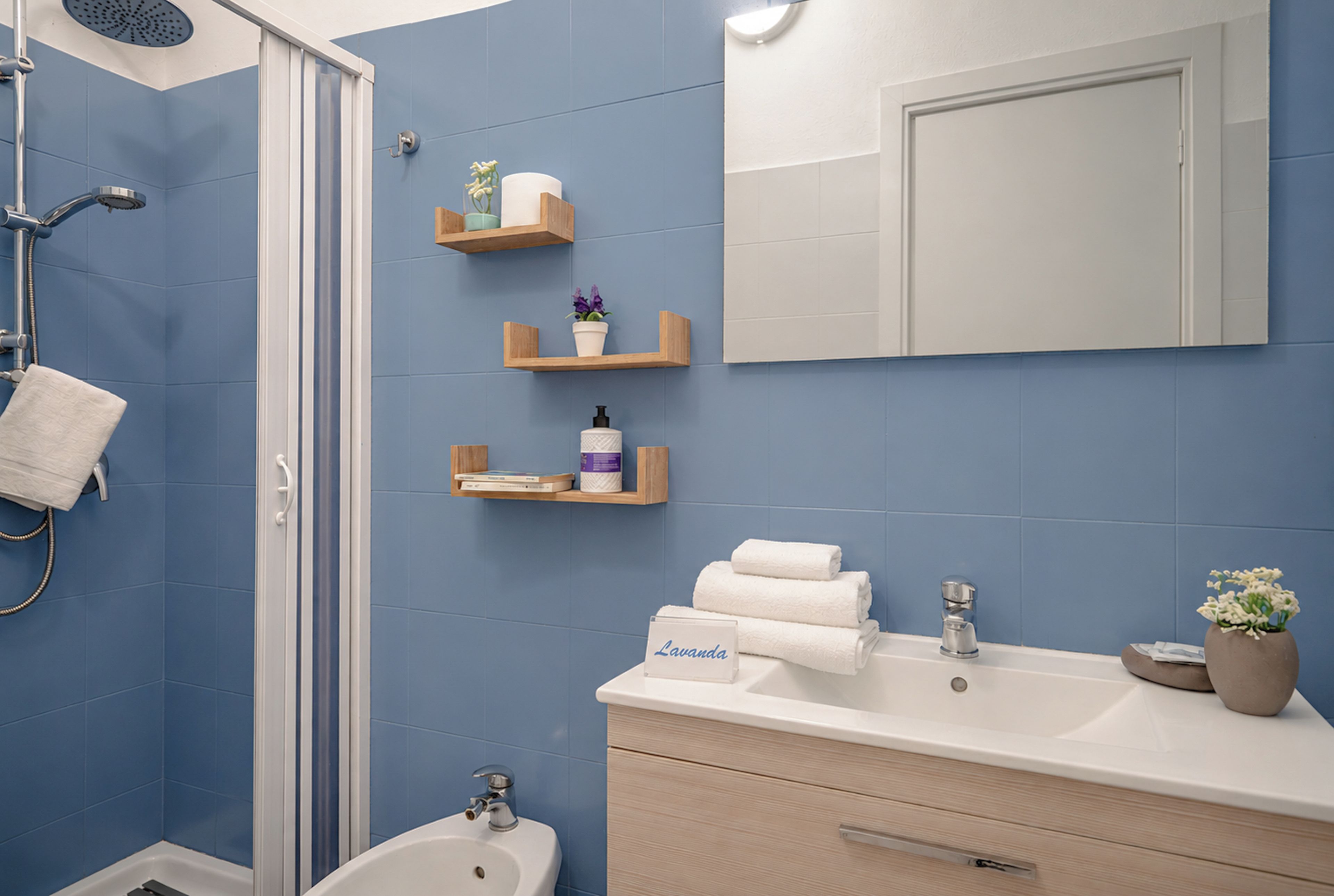 Un bagno con doccia, lavandino e specchio. Asciugamani e articoli da toilette sul ripiano.