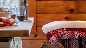 A rustic wooden interior with a wooden table, wine bottle, glasses, and a woven stool. - Northwoods of Lake Geneva. Pet-Friendly! (Williams Bay)
