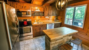 A rustic kitchen with wooden cabinets, a stainless steel refrigerator, a microwave, an oven, a sink, and a large island with stools. - Northwoods of Lake Geneva. Pet-Friendly! (Williams Bay)