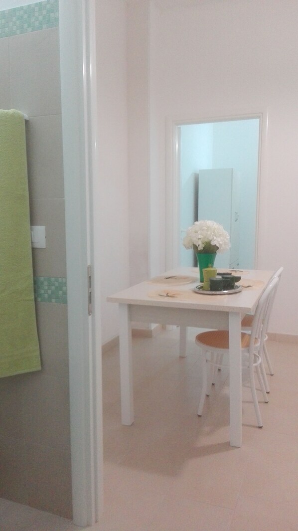 A dining area with a white table, a green vase with white flowers, and a mirror on the wall. - Accommodations 50 meters from the sea, 5 minutes from Gallipoli and the Salentine Maldives (Torre Suda)