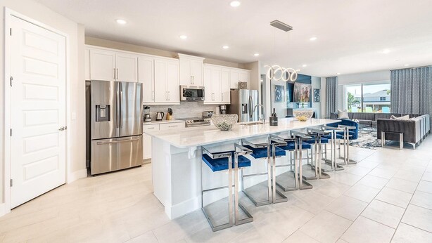 A modern kitchen with stainless steel appliances, a central island with bar stools, and a dining area with a sofa and table. - Energetic Bright Villa With Theater at Encore (Kissimmee)