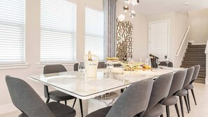 A modern dining area with a glass table, grey upholstered chairs, and a decorative wall piece. - Energetic Bright Villa With Theater at Encore (Kissimmee)