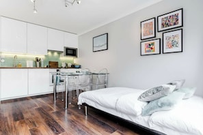 A modern bedroom with a bed, a desk with chairs, and a kitchen area. - Beautifully Presented 2BD Flat near Westminster (London)