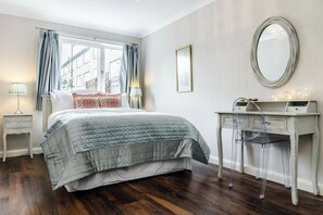 A bedroom with a bed, a dresser, a mirror, and a window with curtains. - Beautifully Presented 2BD Flat near Westminster (London)