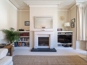 A living room with a fireplace, bookshelves, a television, and a mirror. - Inviting 2BD Victorian Flat, Near Hampstead (London)