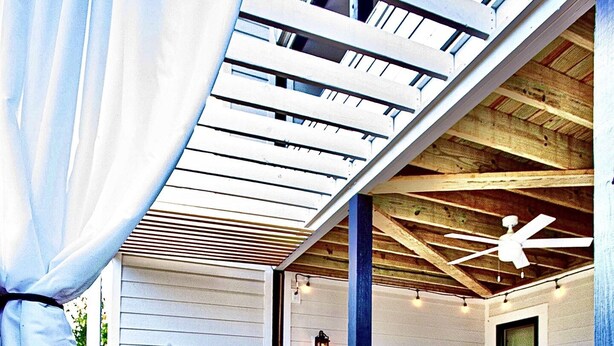 Ein überdachter Außenbereich mit Holzterrasse, Whirlpool und Sitzgelegenheiten unter einer Pergola.