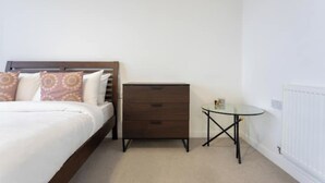 Een slaapkamer met een bed, een dressoir en een klein tafeltje.