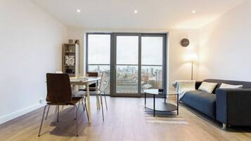 A modern living room with a sofa, a dining table with chairs, and a view through a large window.