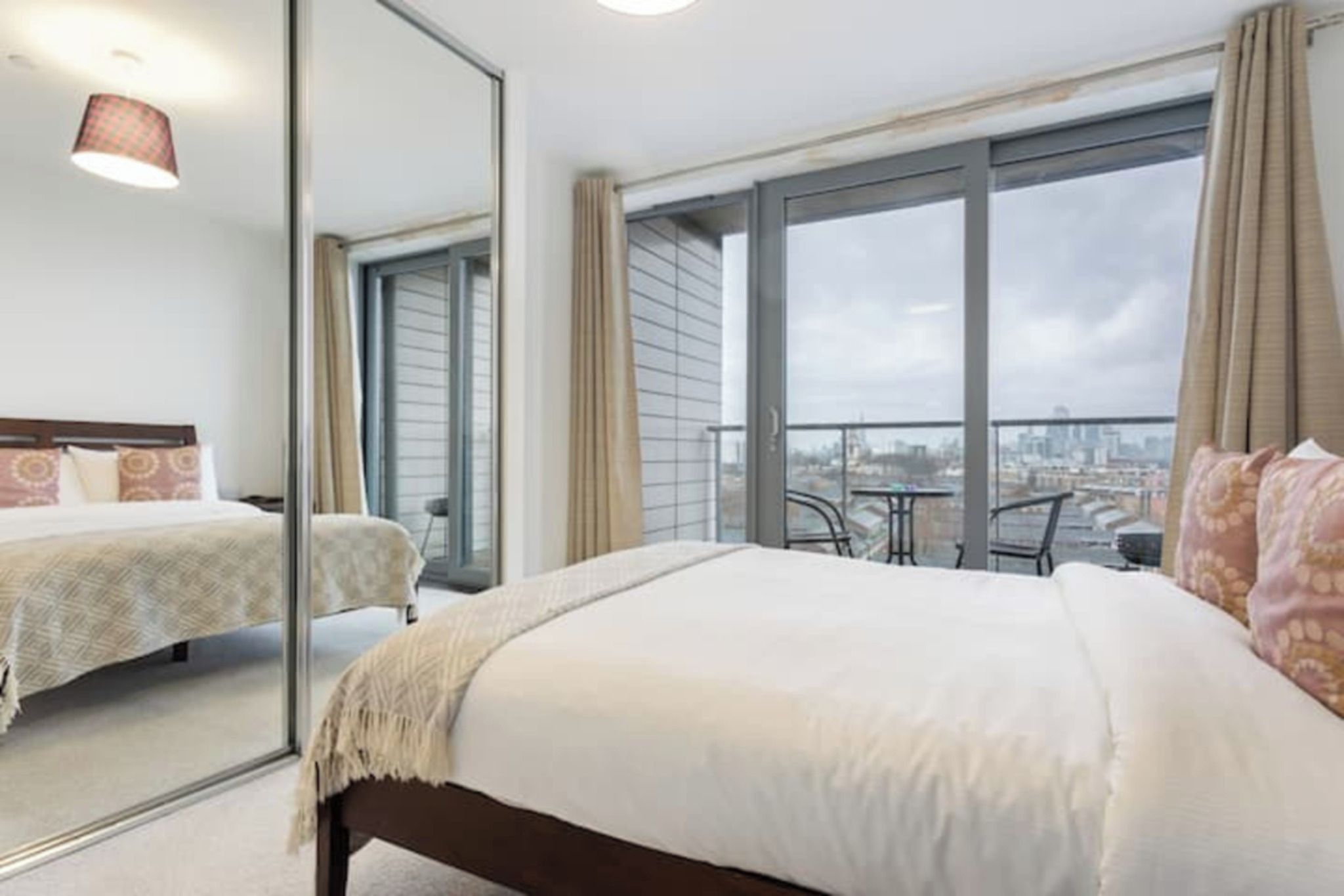 A hotel room with a large bed, a balcony with a table and chairs, and a city view.